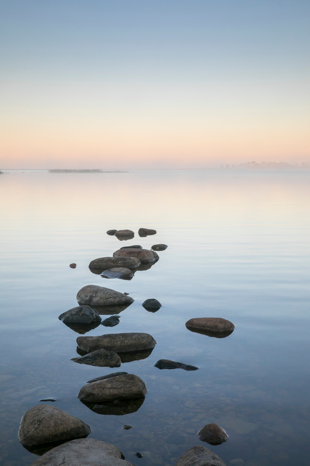 A lighthouse with waves coming up the sand on the beach and clouds in a blue sky.